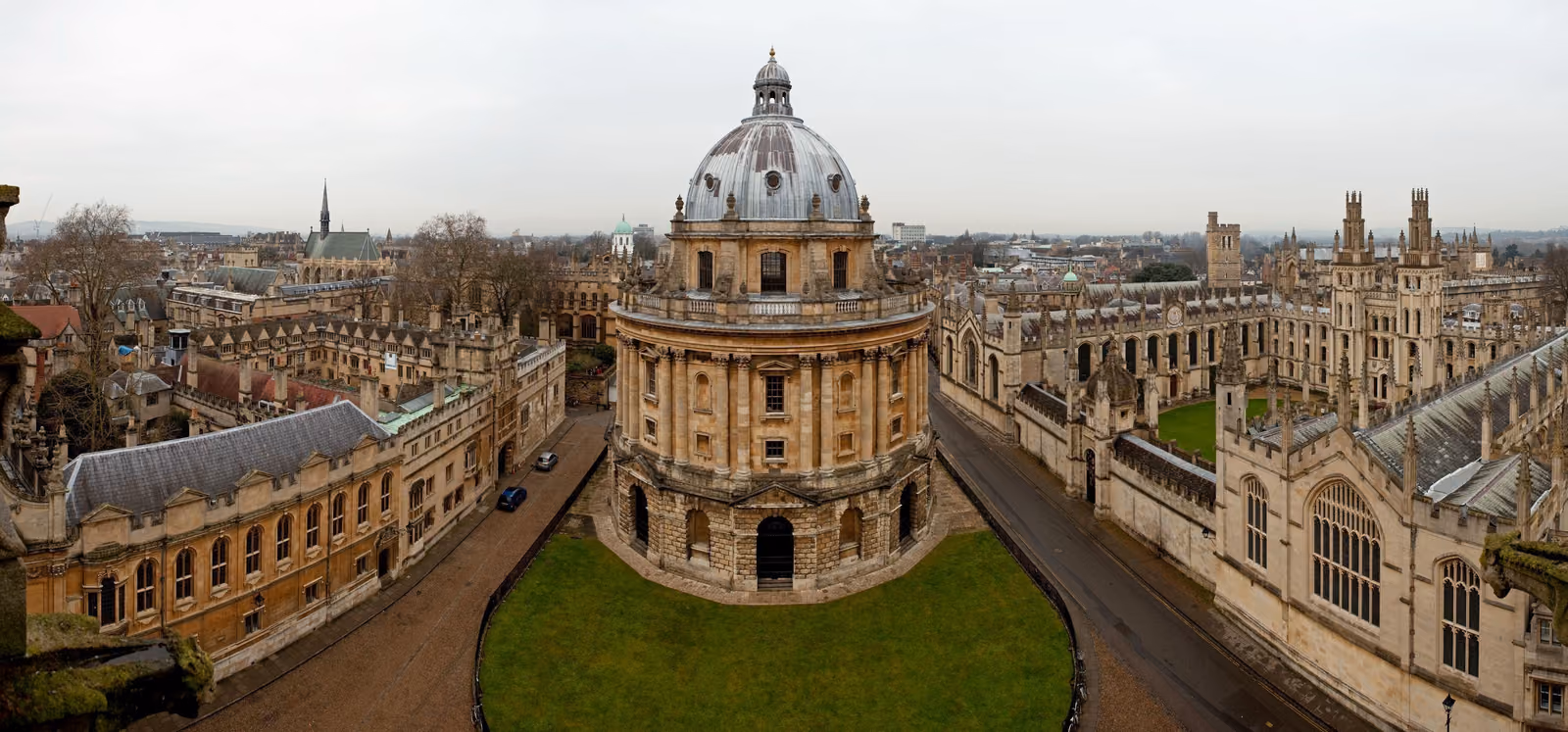 A panoramic rooftop view of central Oxford with the Radcliffe Camera's dome at the centre, ringed by college spires.