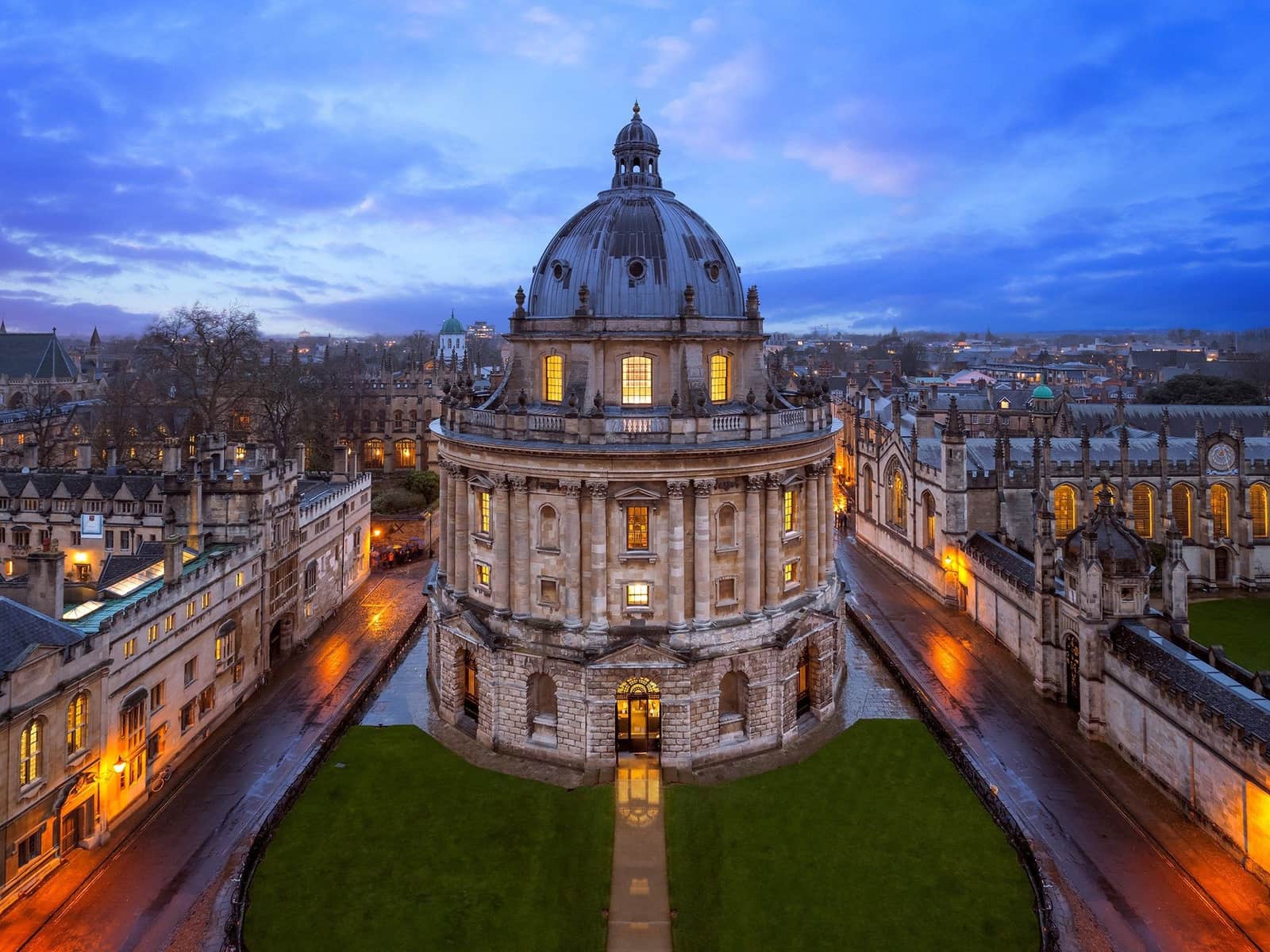 The Radcliffe Camera's illuminated domed rotunda at dusk, viewed across Radcliffe Square in Oxford.