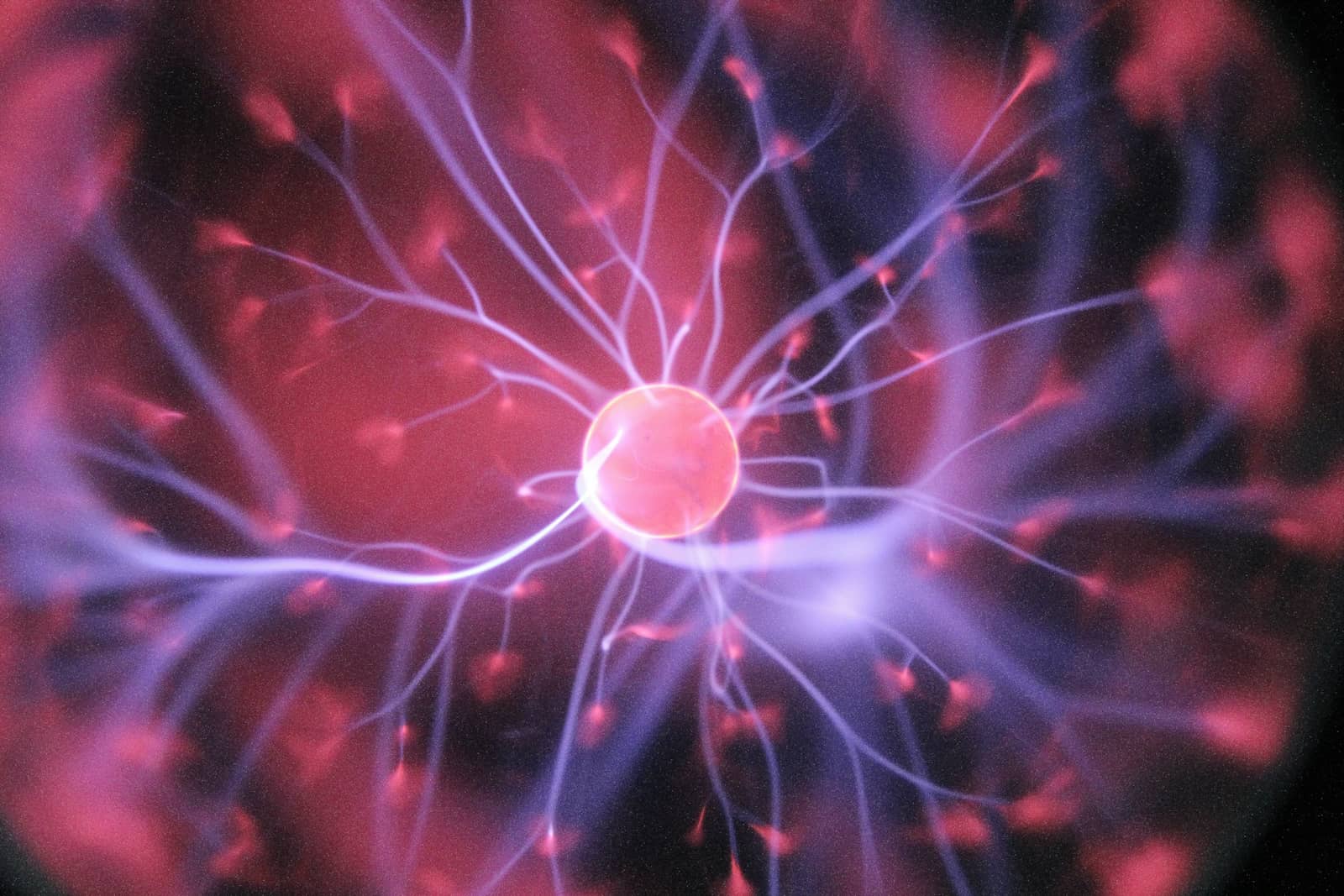 A glowing plasma ball with pink and blue electrical filaments radiating from a bright central sphere.
