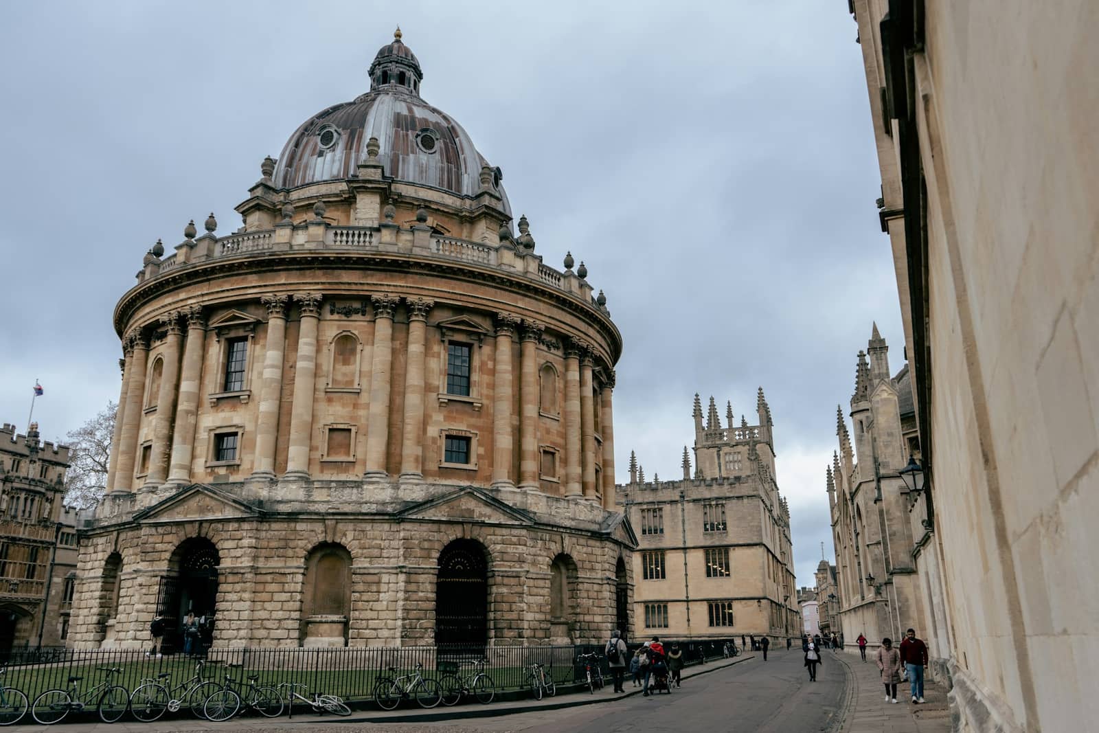 The rotunda of Oxford's Radcliffe Camera on a grey day, with college buildings and spires lining the street behind it.