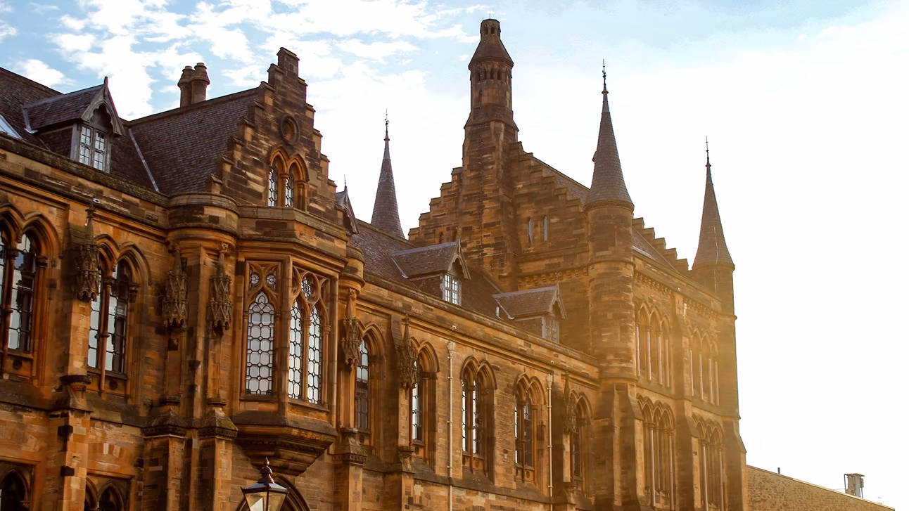 A Gothic sandstone university building with spires and arched windows lit by low golden sunlight