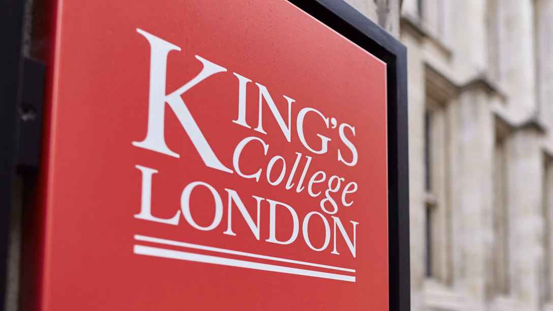 A red King’s College London sign mounted outside a stone campus building on the Strand